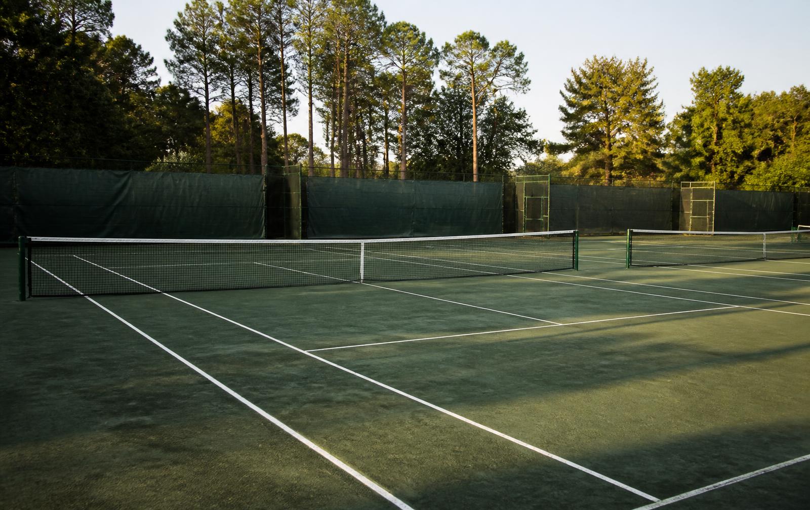 Freshly groomed green clay tennis courts framed by tall pines