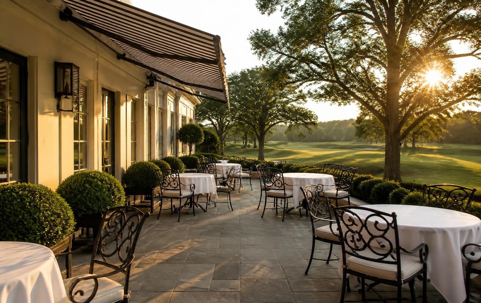 A club terrace with linen-topped dining tables overlooking the golf course at golden hour
