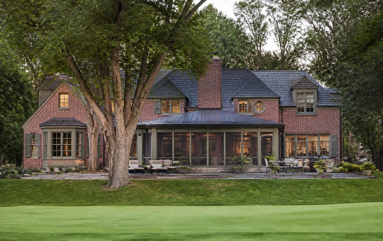 The rear elevation of a brick home with a screened porch seen from across a fairway