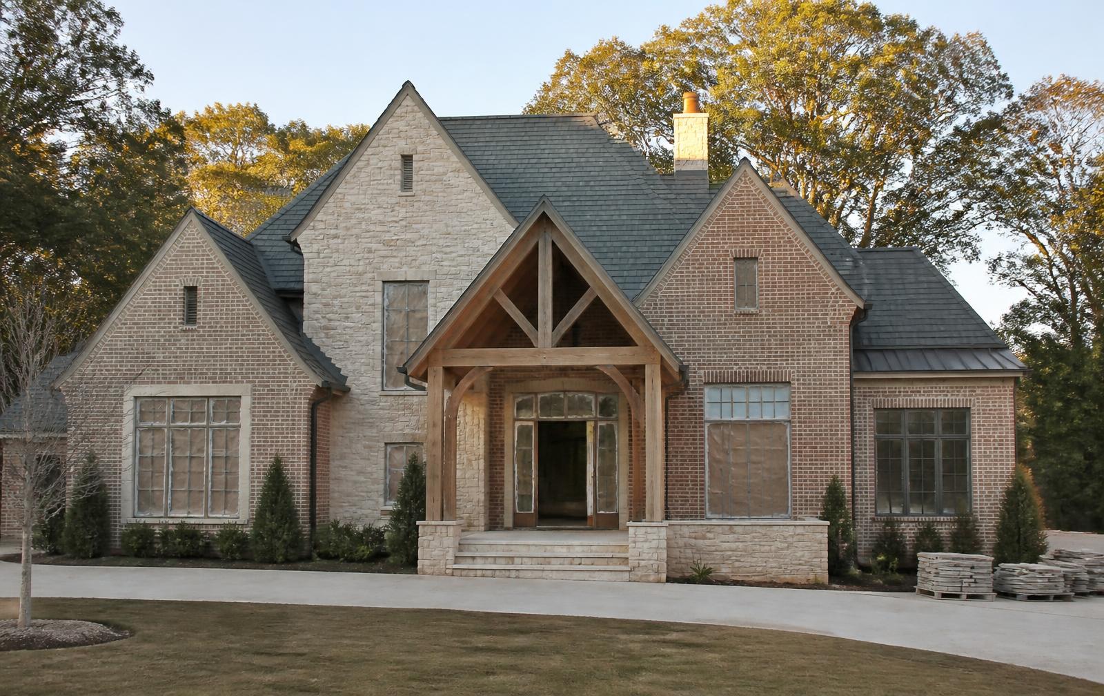A custom brick and limestone home nearing completion with a timber-framed entry porch