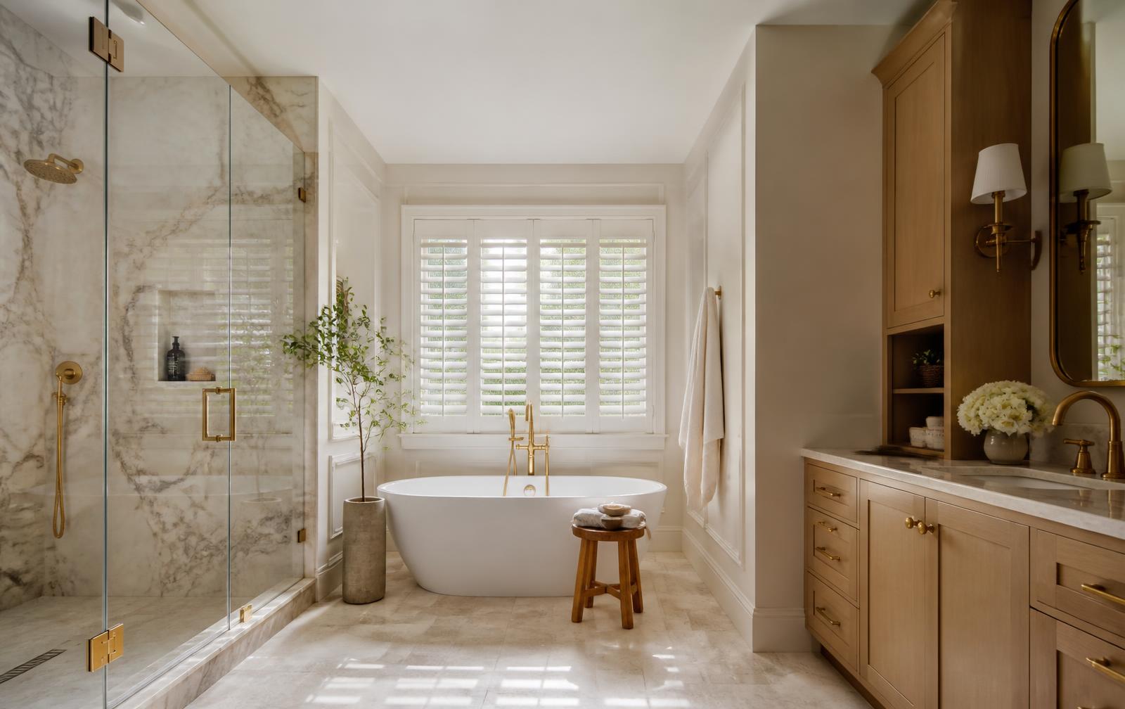 A renovated primary bathroom with a marble shower, freestanding tub, and brass fittings